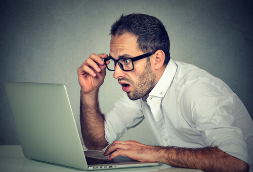 man in glasses with a shocked look on his face staring at computuer screen