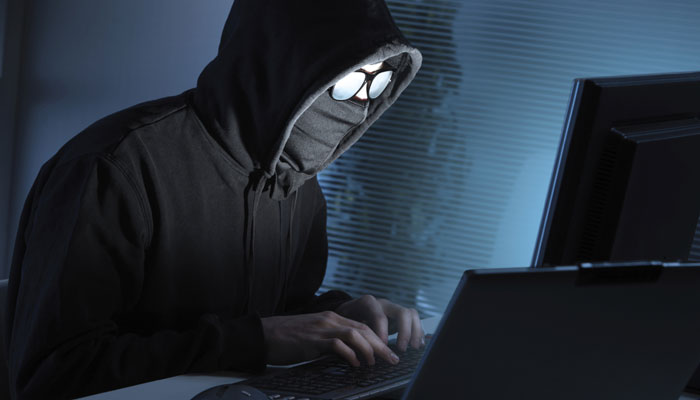 Hacker at work with face covered by hoodie and dark glasses